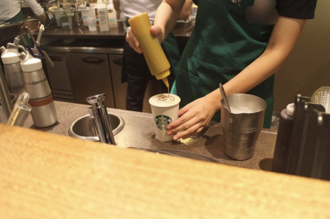 キャラメルソースをかけるスタバ店員